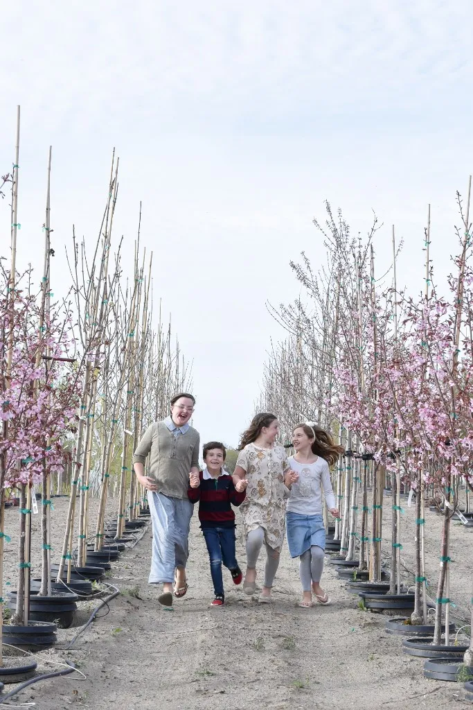 Children running down a path between blooming nursery trees